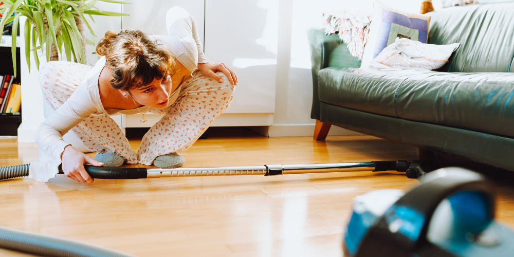 Woman cleaning underneath a sofa using a vacuum cleaner