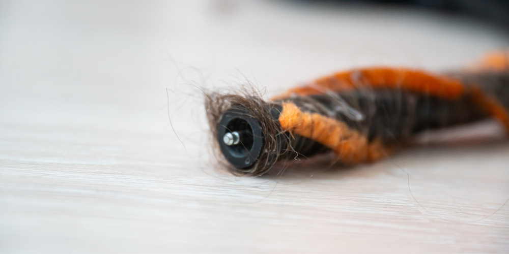 Close-up of a vacuum cleaner's brush bar with some matted hair caught in the bristles