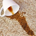 A cup of coffee spilled on a light beige, cream carpet