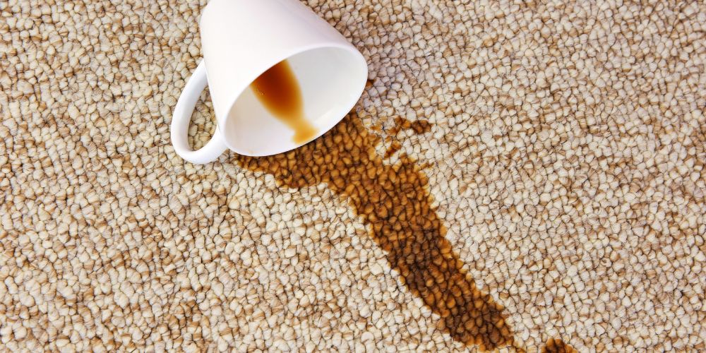 A cup of coffee spilled on a light beige, cream carpet